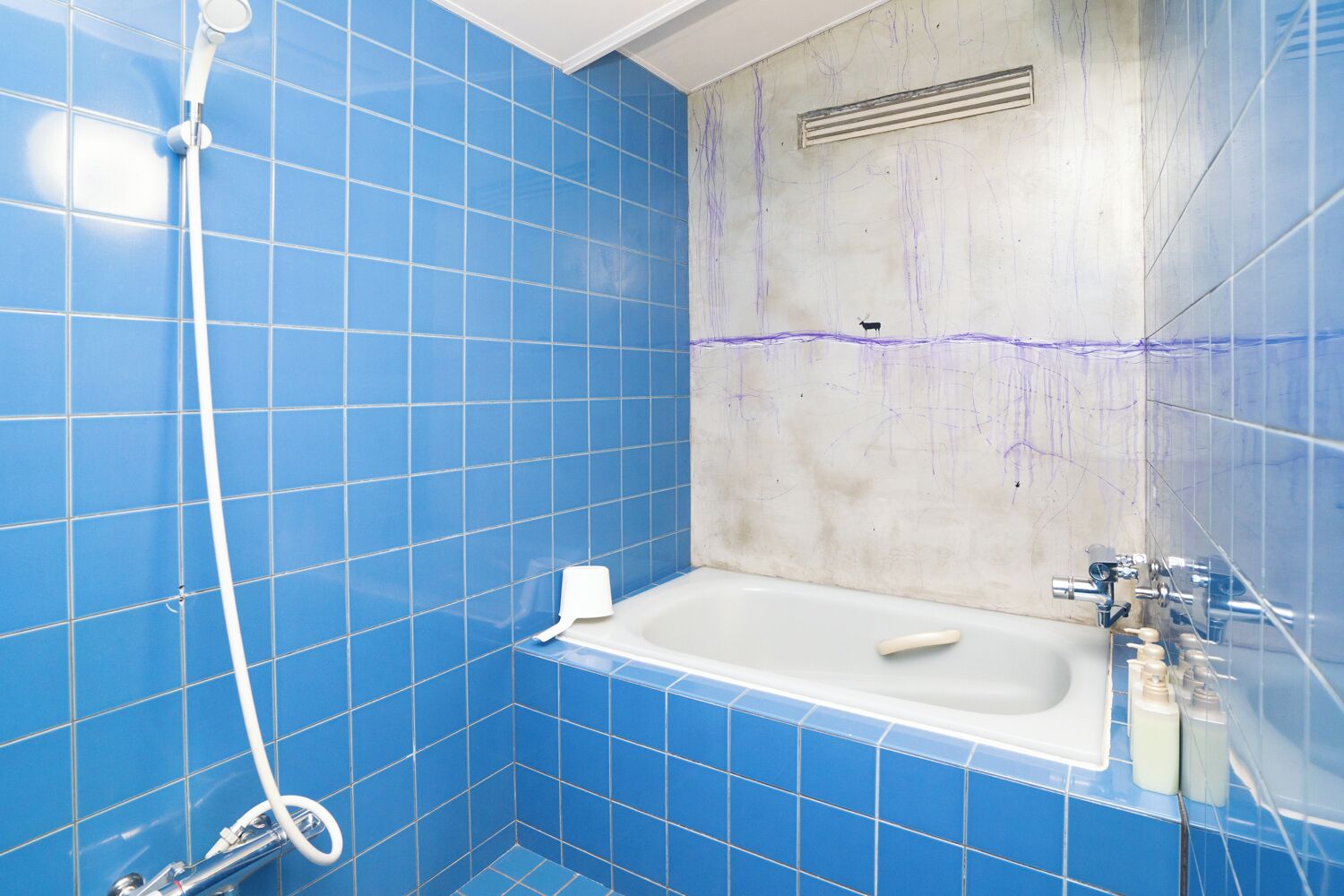 A bathroom with blue tiles, a white bathtub, and a shower head.