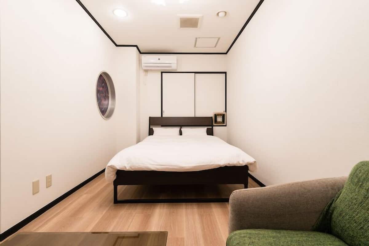 Un dormitorio pequeño y moderno con cama, una silla verde y aire acondicionado instalado en la pared.