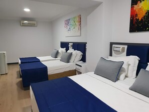 A hotel room with two beds, each with a blue bedspread and white linens, a small bedside table, and a wall-mounted air conditioner.