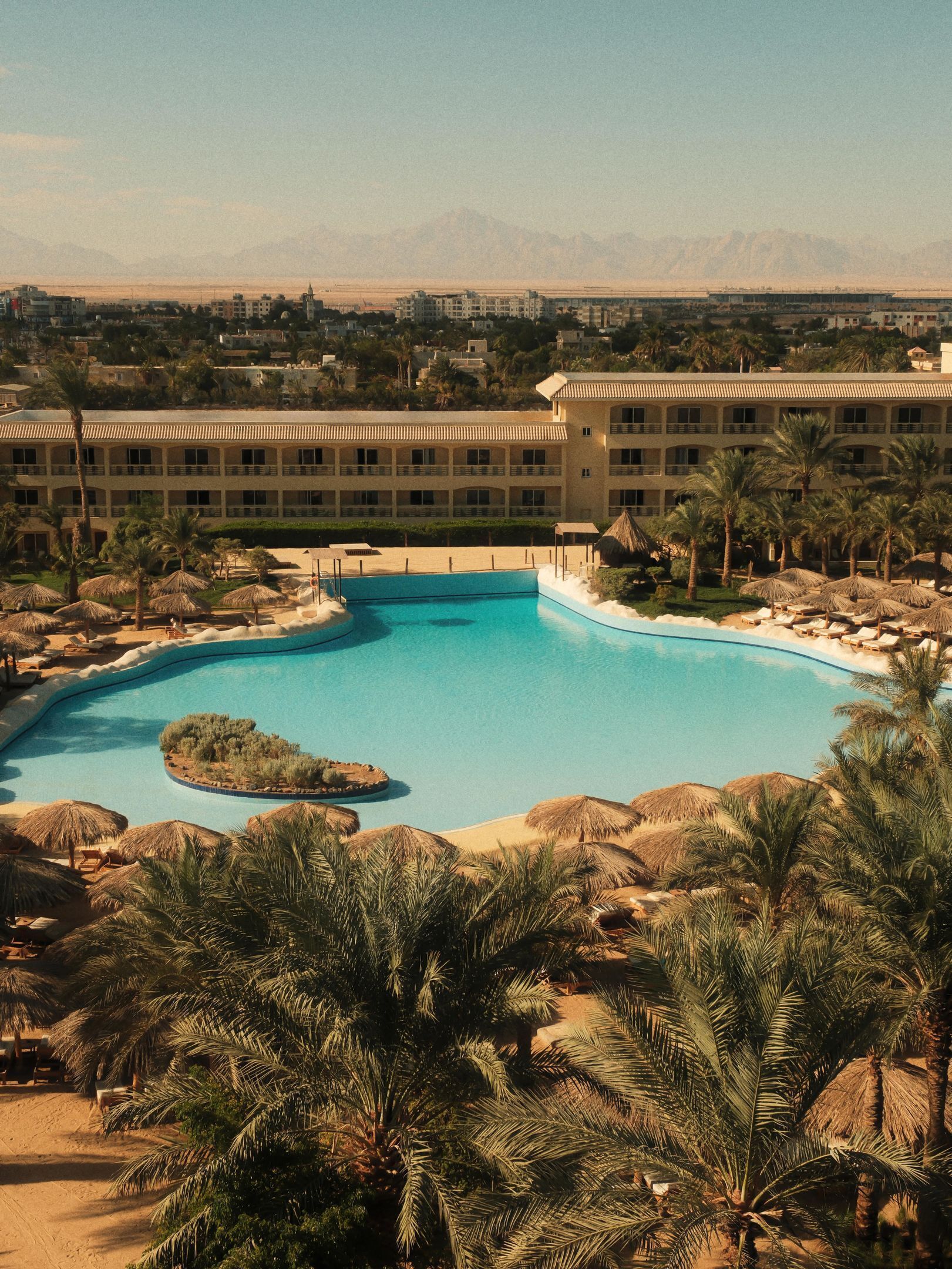 A resort with a large swimming pool, palm trees, and a hotel building in the background.