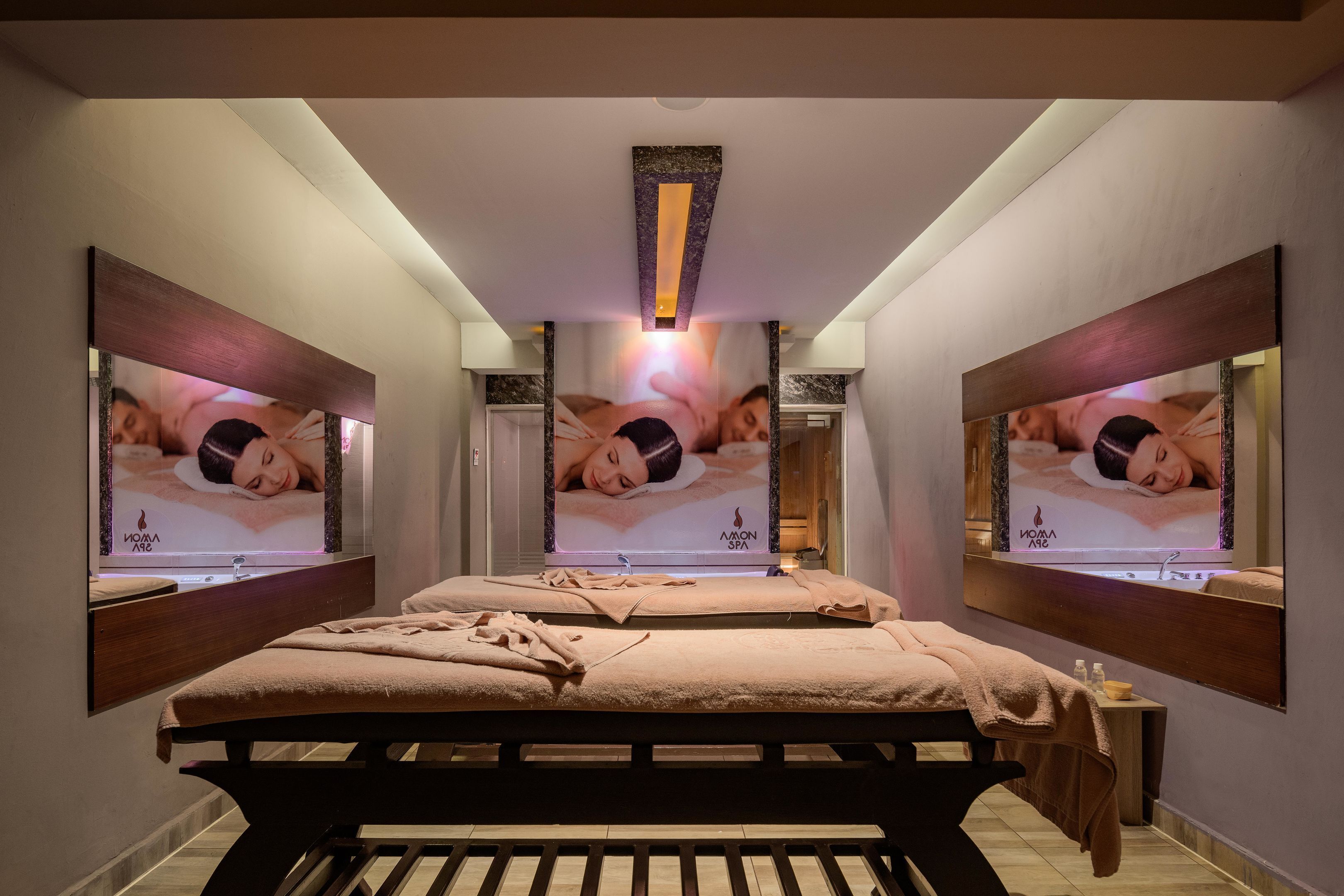 Ein Spa-Raum mit zwei Betten, einem großen Spiegel und einem an der Wand montierten Fernseher, der Wellness-Inhalte anzeigt.