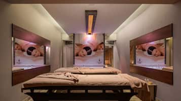 Ein Spa-Raum mit zwei Betten, einem großen Spiegel und einem an der Wand montierten Fernseher, der Wellness-Inhalte anzeigt.