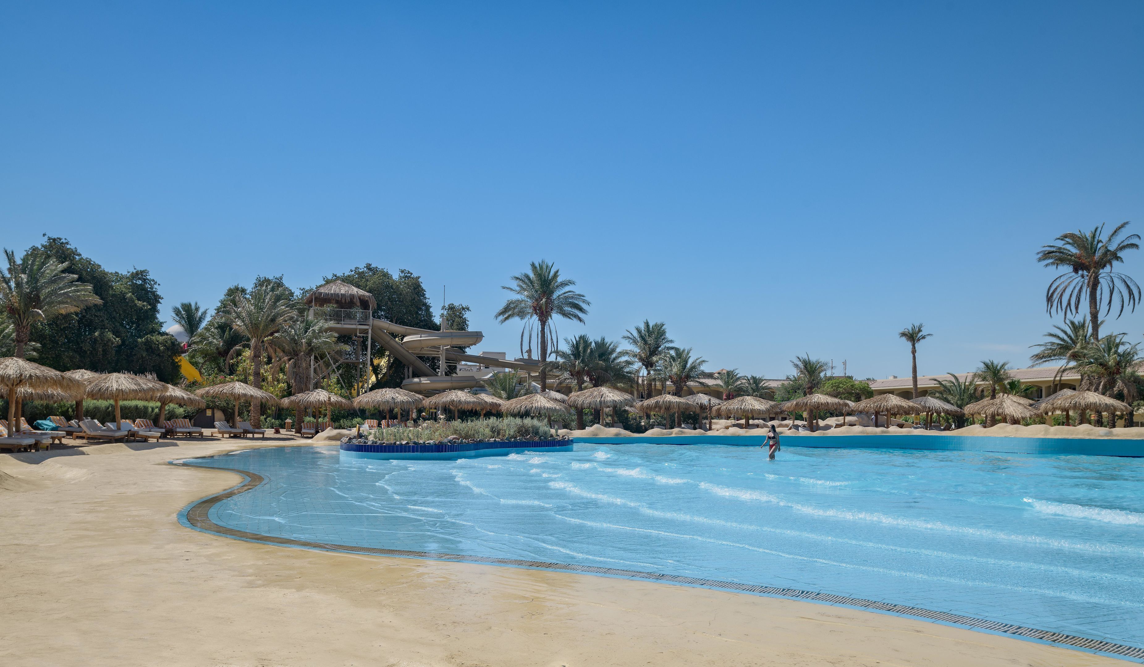 A resort pool with palm trees, lounge chairs, and a water slide.