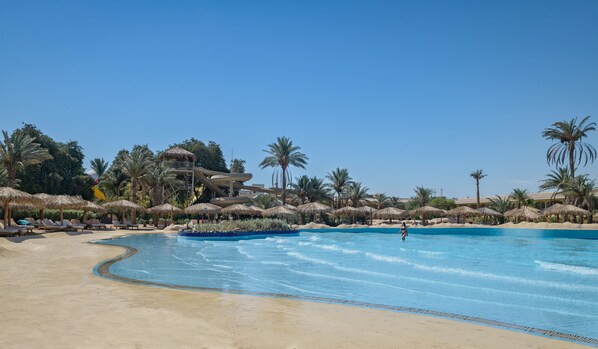 A resort pool with palm trees, lounge chairs, and a water slide.
