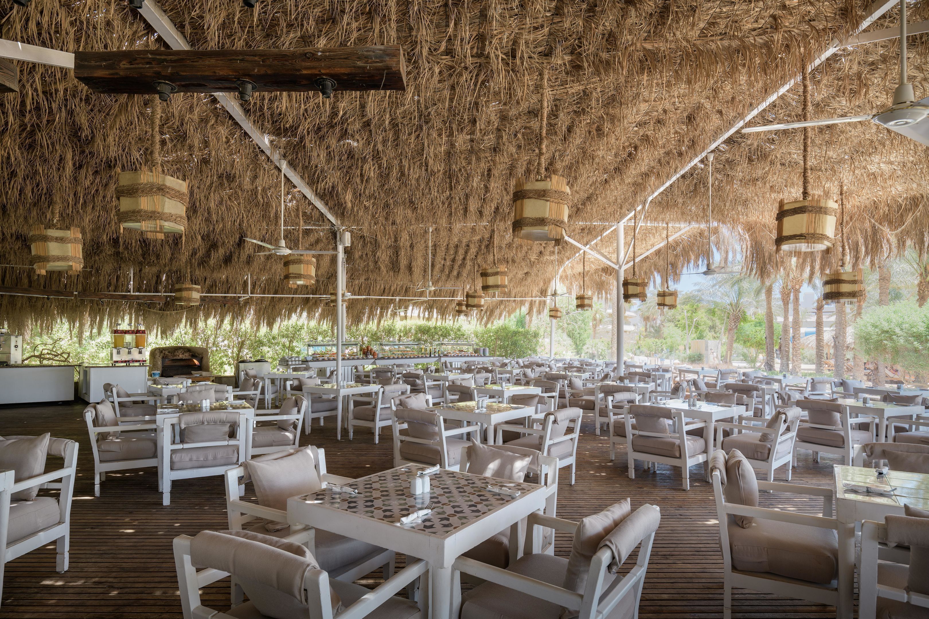 An outdoor dining area with white tables and chairs, a thatched roof, and hanging light fixtures.