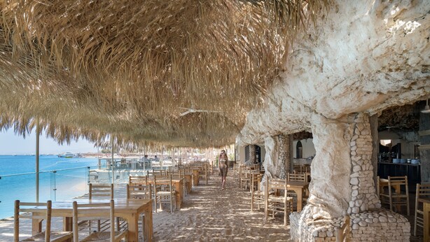 A beachside restaurant with outdoor seating, a thatched roof, and a view of the ocean. - Sindbad Club (Hurghada)