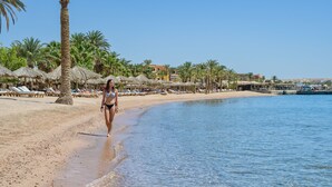 A beach with palm trees, sun loungers, and a clear blue sky. - Sindbad Club (Hurghada)