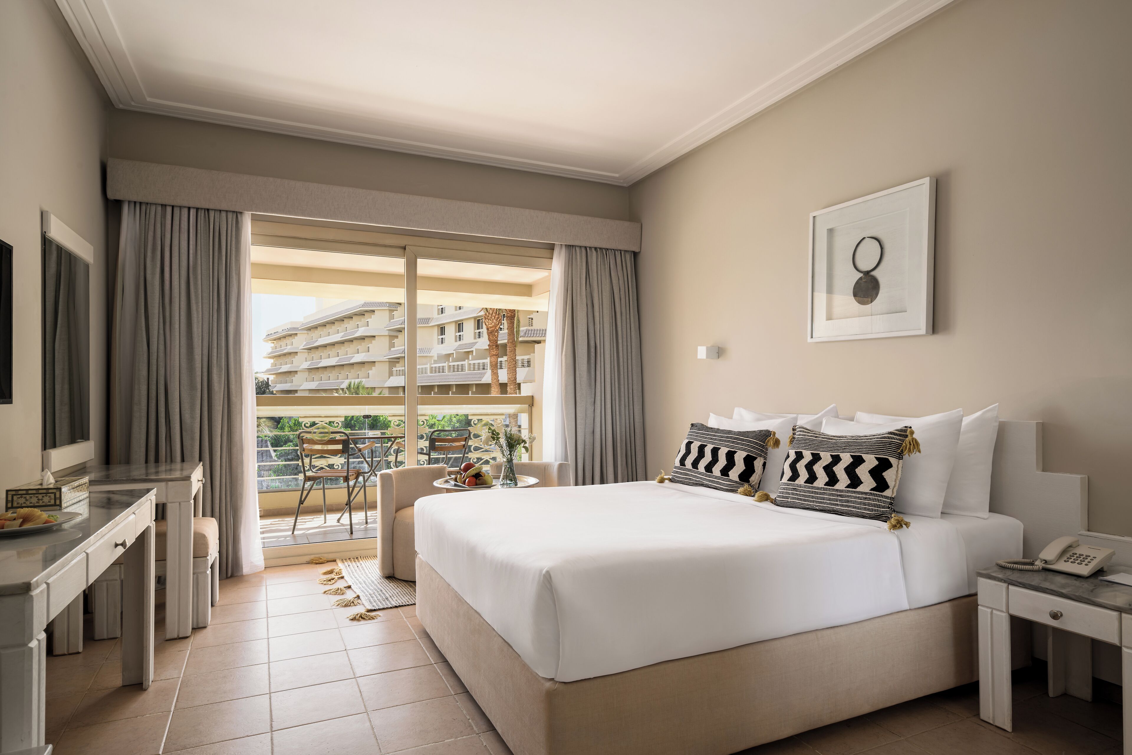 Ein Hotelzimmer mit Bett, Schreibtisch, Stuhl und einem Balkon mit Blick auf Gebäude.
