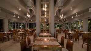 A spacious dining area with multiple tables and chairs, large windows, and hanging pendant lights.