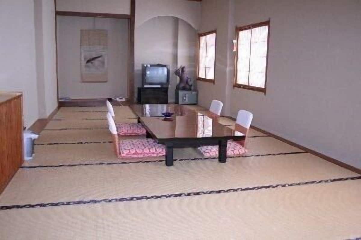 A traditional tatami mat room with a low table and chairs, a television, and a small cabinet.