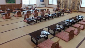 Un salón de conferencias con varias mesas y sillas, ventanas amplias y decoración tradicional.