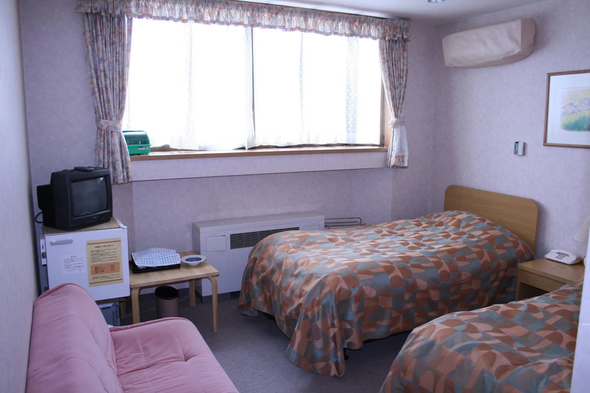 A hotel room with two beds, a desk with a computer, a television, and a window with curtains.