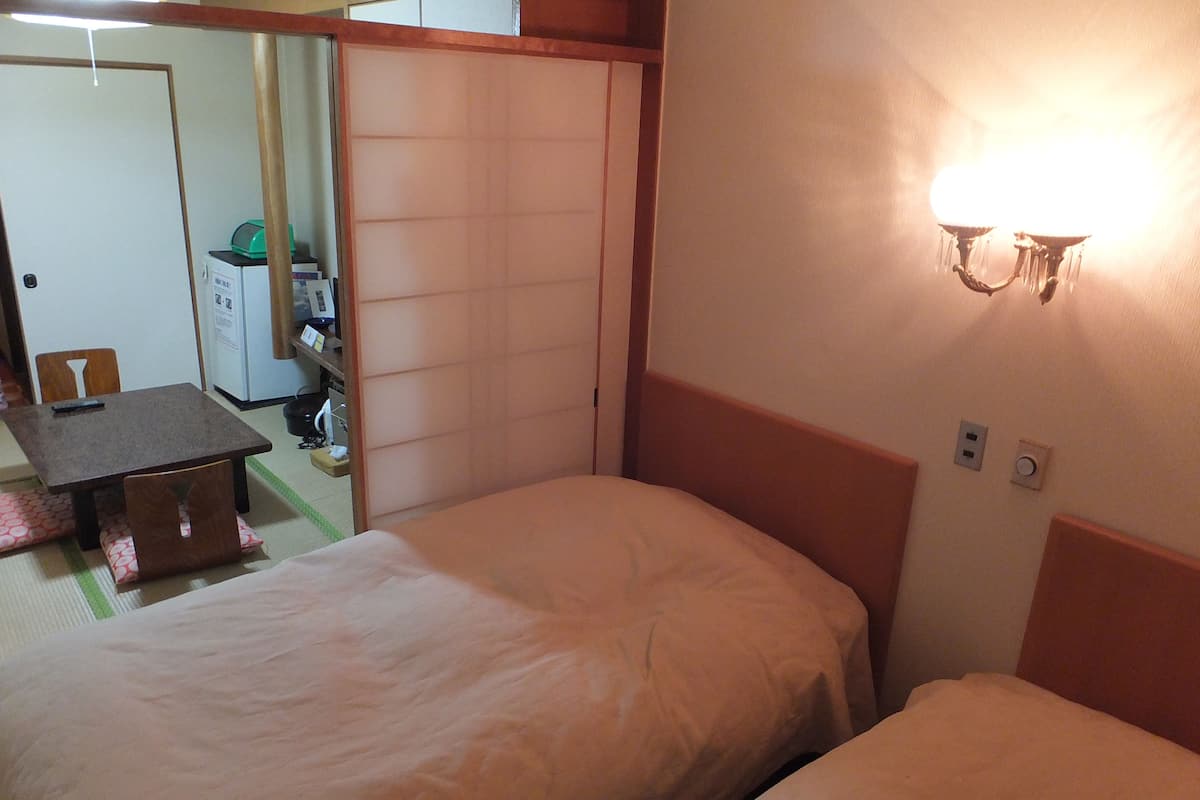 A hotel room with two beds, a small table, a chair, a desk, and a wardrobe.