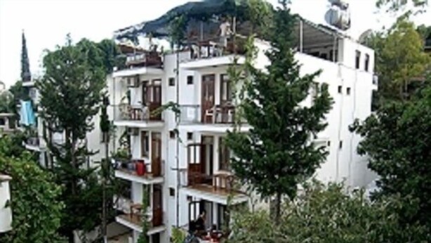 Un edificio de varios pisos con balcones y un paisaje montañoso al fondo.