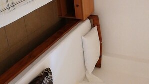 Habitación compacta con cama individual, cabecera de madera, un pequeño mueble de madera y un enchufe en la pared.