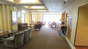 A hotel lobby with a carpeted floor, seating areas with sofas and chairs, a reception desk, and a large window providing natural light. - Tsuyama Grand Hotel (Tsuyama)