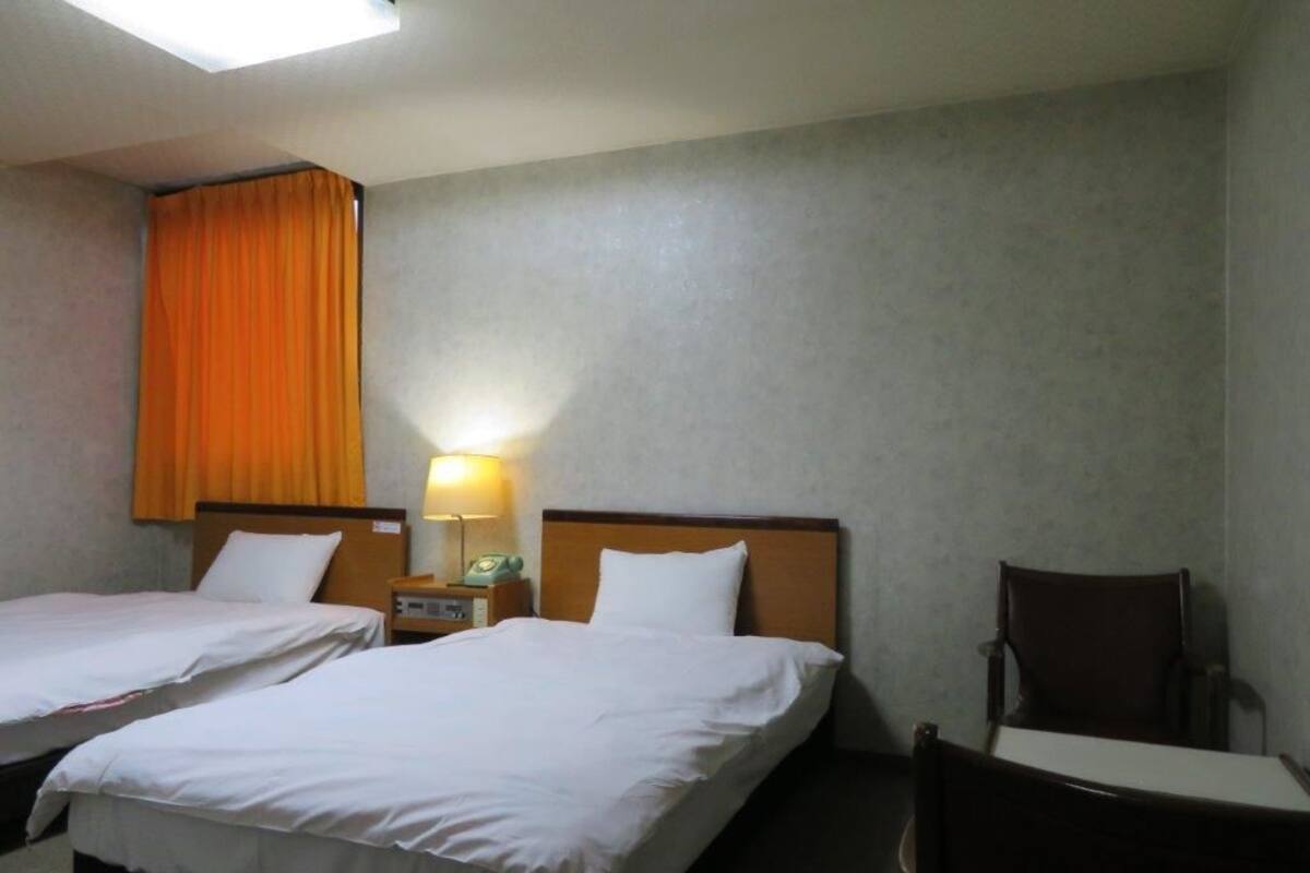 Une chambre d’hôtel avec deux lits, un bureau, une chaise, une lampe et une fenêtre avec des rideaux.