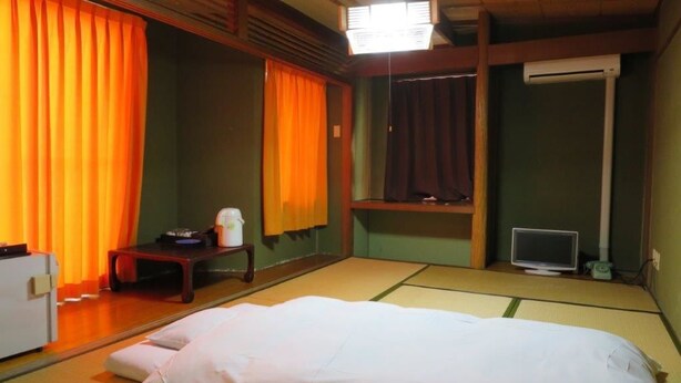 A traditional Japanese room with tatami flooring, a bed with white bedding, a television, and a small table with a kettle. - Tsuyama Grand Hotel (Tsuyama)