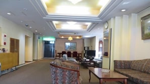 A hotel lobby with a reception desk, seating area, and a television. - Tsuyama Grand Hotel (Tsuyama)