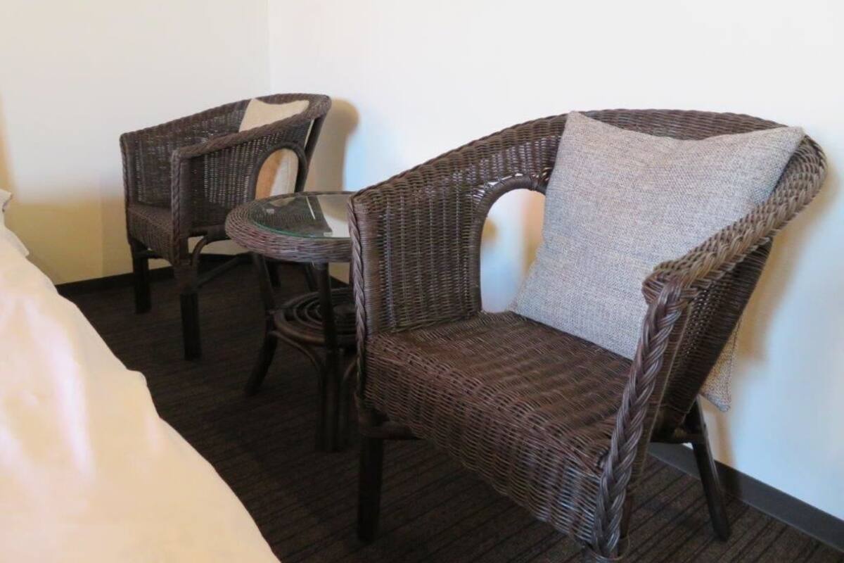 Une chaise en osier avec un coussin et une table en verre dans une chambre d’hôtel.