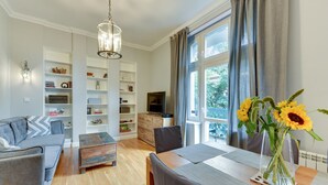 A modern living room with a sofa, dining table, chairs, a bookshelf, and a TV. - Oxford Family apartment in a quiet Sopot townhouse by Lion Apartments (Sopot)