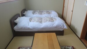 Een kleine kamer met twee bedden, een houten tafel, tatami matten en een shoji scherm.
