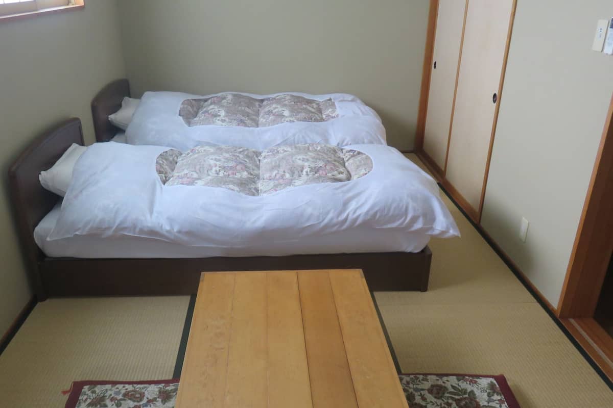 Um quarto pequeno com duas camas, uma mesa de madeira, esteiras de tatame e um painel shoji.