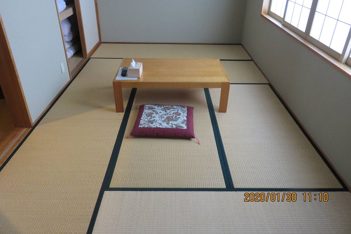 Um quarto com esteira de tatame, uma mesa de madeira, um travesseiro e uma caixa de lenços.