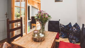 Une table de salle à manger en bois, ornée d’un vase de fleurs, d’un panier rempli d’œufs et d’un coussin rouge.