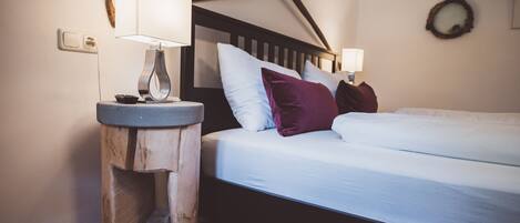 Een slaapkamer met een houten hoofdbord, een nachtkastje met een lamp, en een bed met witte beddengoed en een paars kussen.