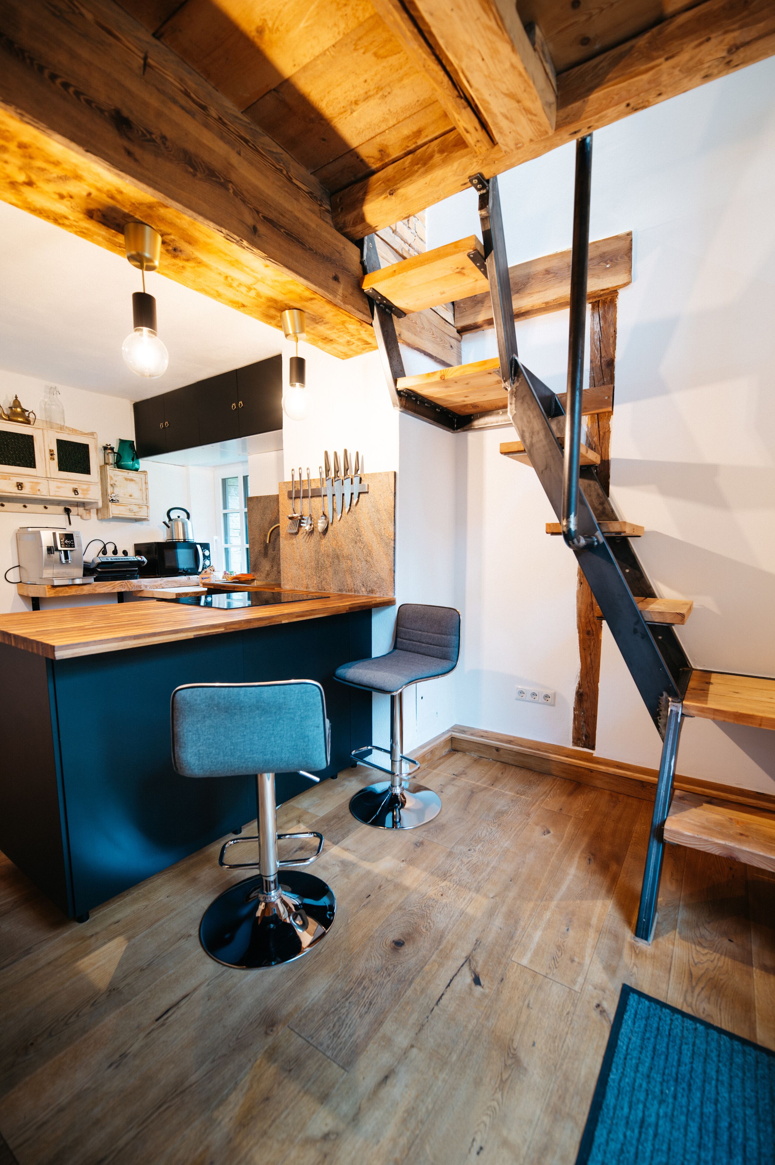 Una cocina con vigas de madera, una zona de bar con taburetes y una escalera.