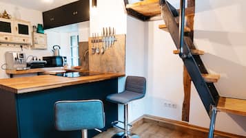 Una cocina con vigas de madera, una zona de bar con taburetes y una escalera.