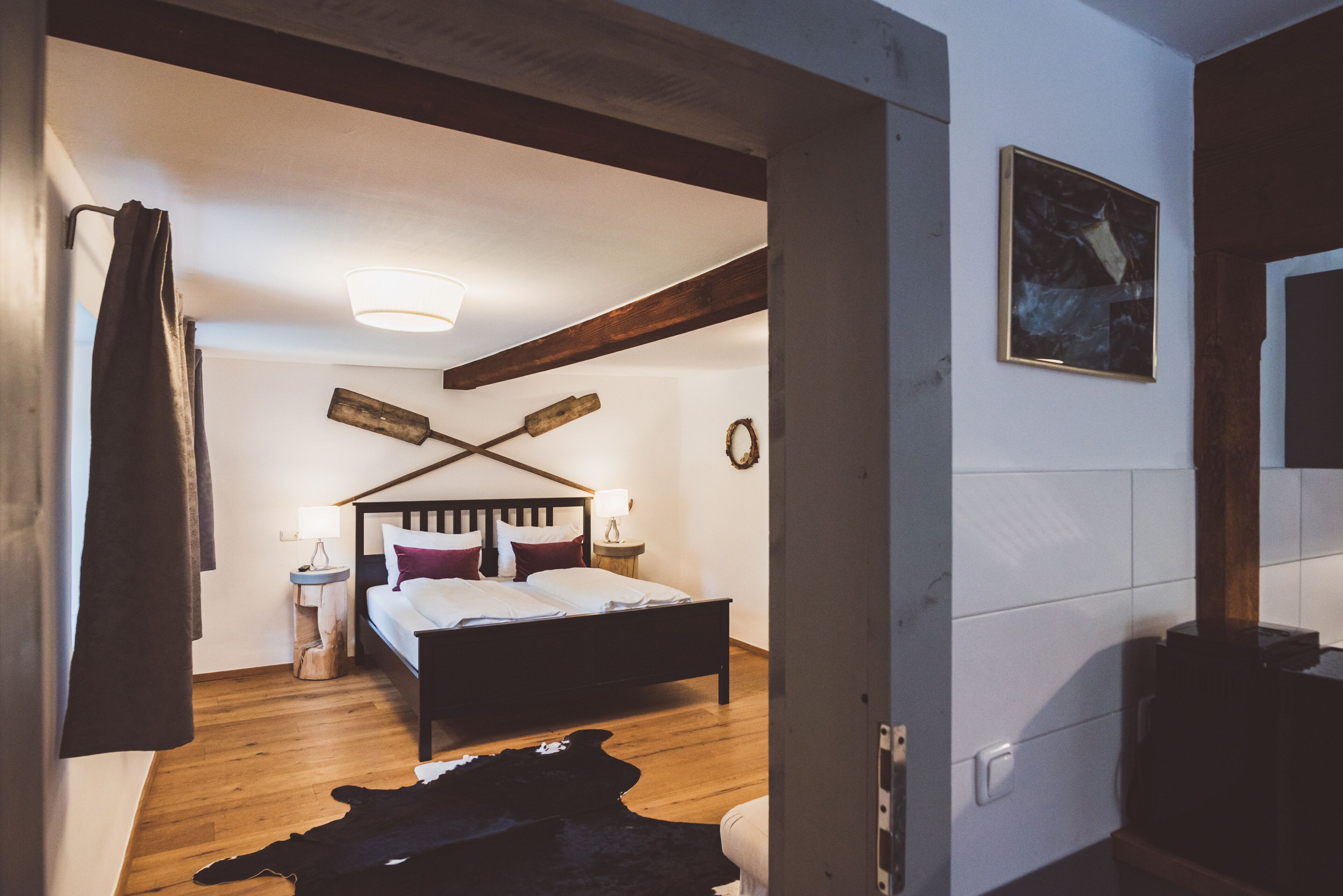 Ein Schlafzimmer mit einem hölzernen Bett, einem Nachttisch, einer Lampe, einem Kuhfellteppich und einem Bild an der Wand.