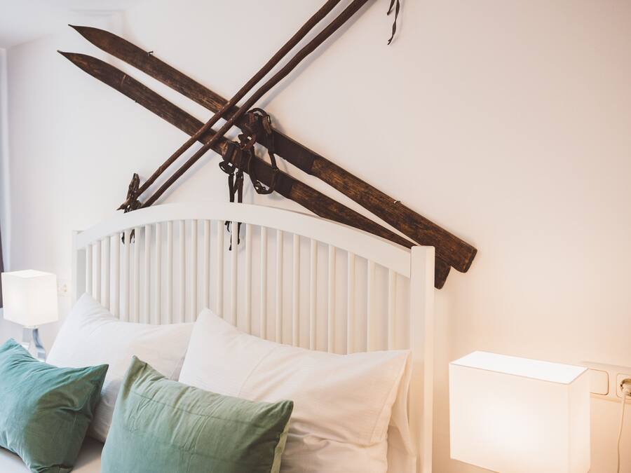 Ein Bett mit weißer Bettwäsche und grünen Kissen, eine Nachttischlampe und ein rustikales Holz-Kopfende, an dem Skier befestigt sind.