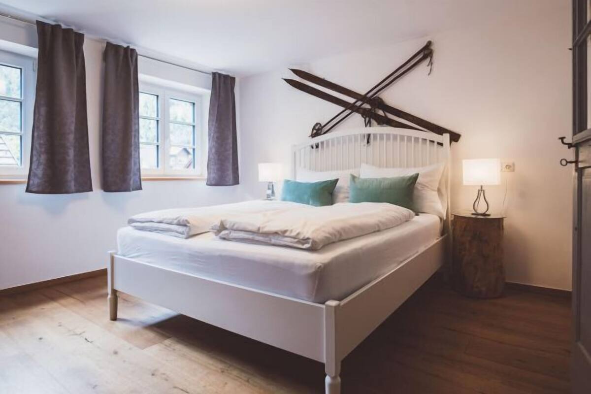 A bedroom with a bed, a window with curtains, a bedside table with a lamp, and a radiator.