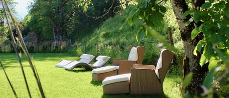 A grassy outdoor area with wicker furniture, including chairs and a sofa, and a tree in the background.