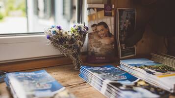 A wooden table with a vase of flowers, a stack of brochures, and a framed photo on a window sill.