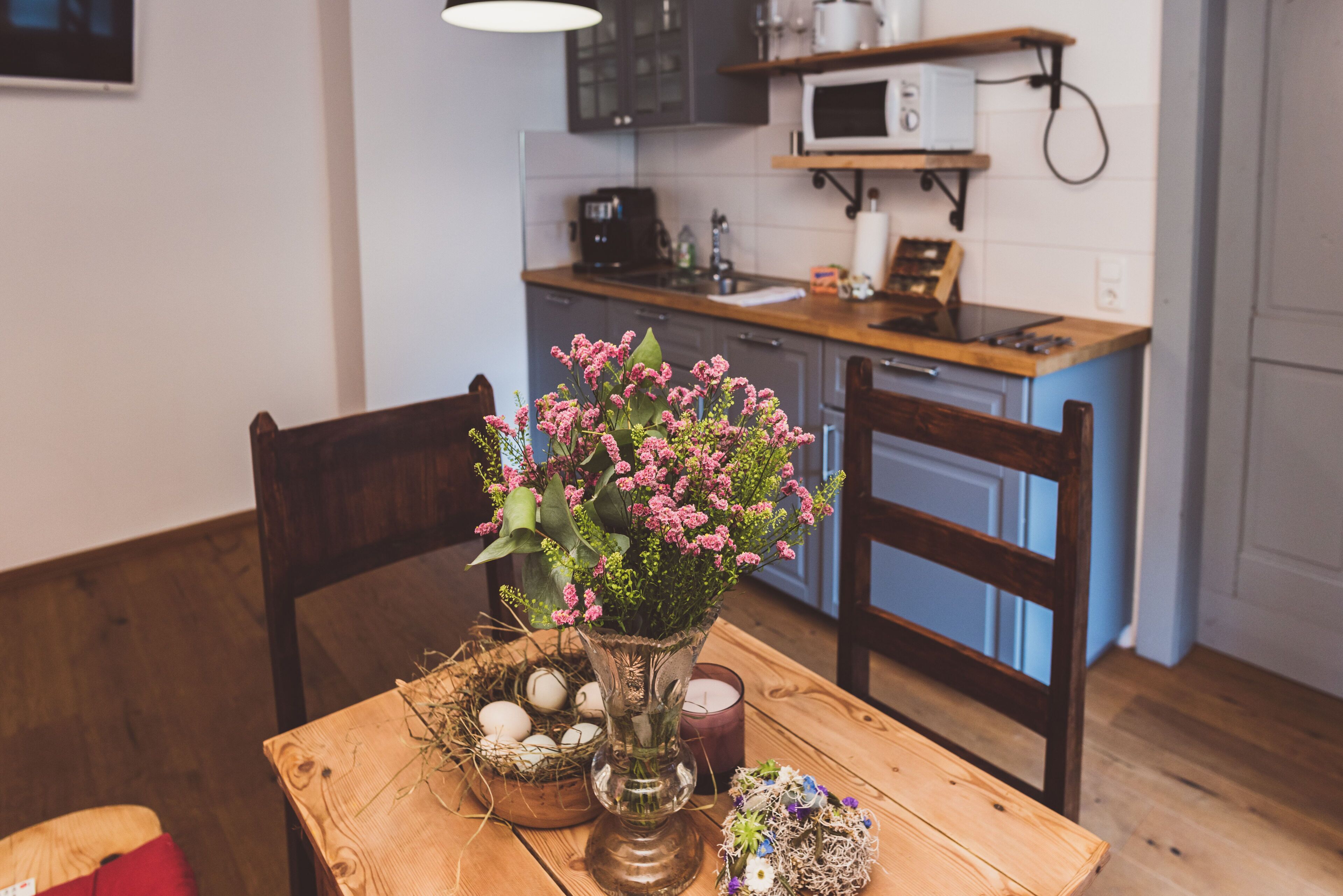 Una mesa de madera para comer con un florero, una vela y un nido con huevos.