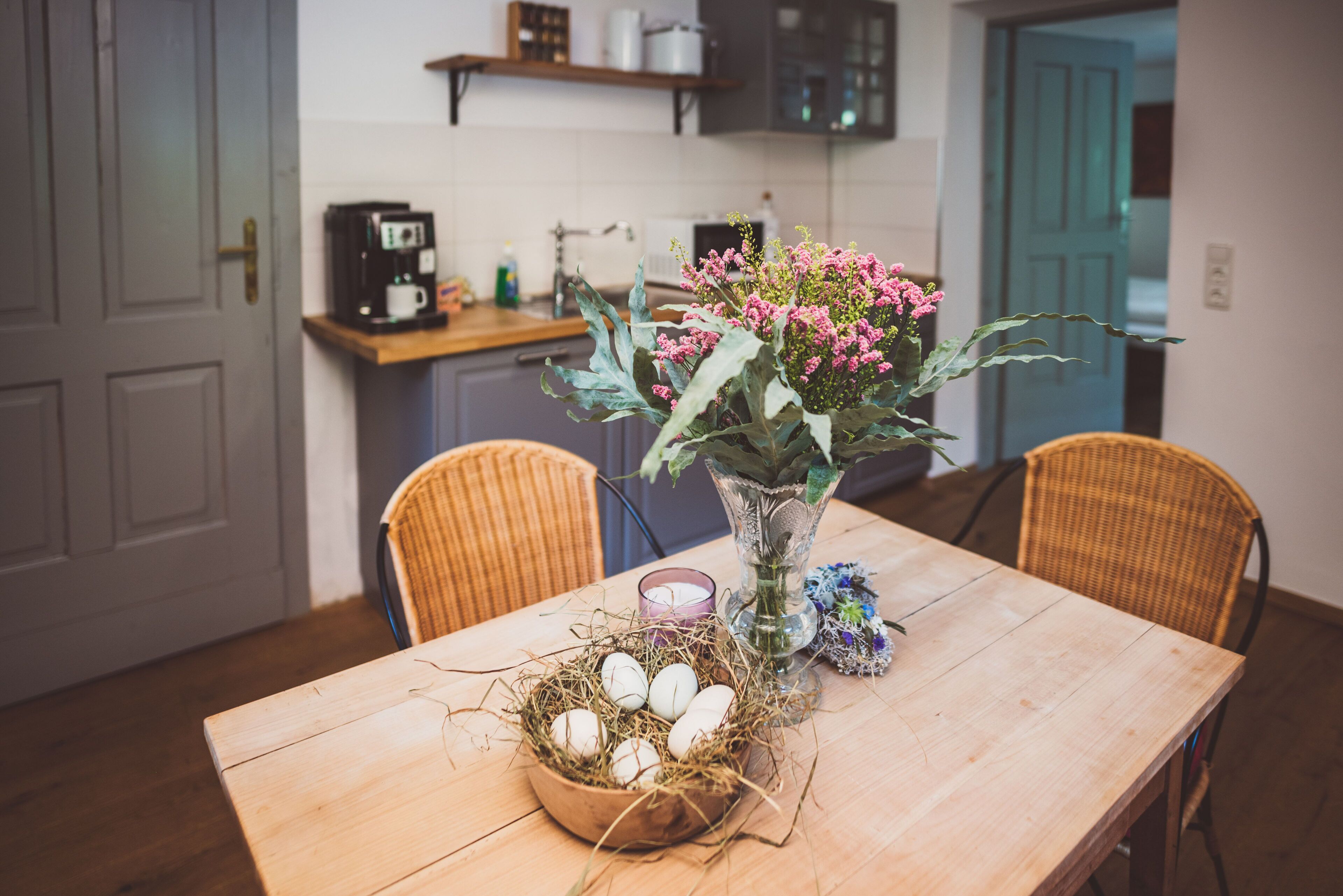 Una mesa de comedor con un nido que contiene huevos, un florero con flores y una vela.