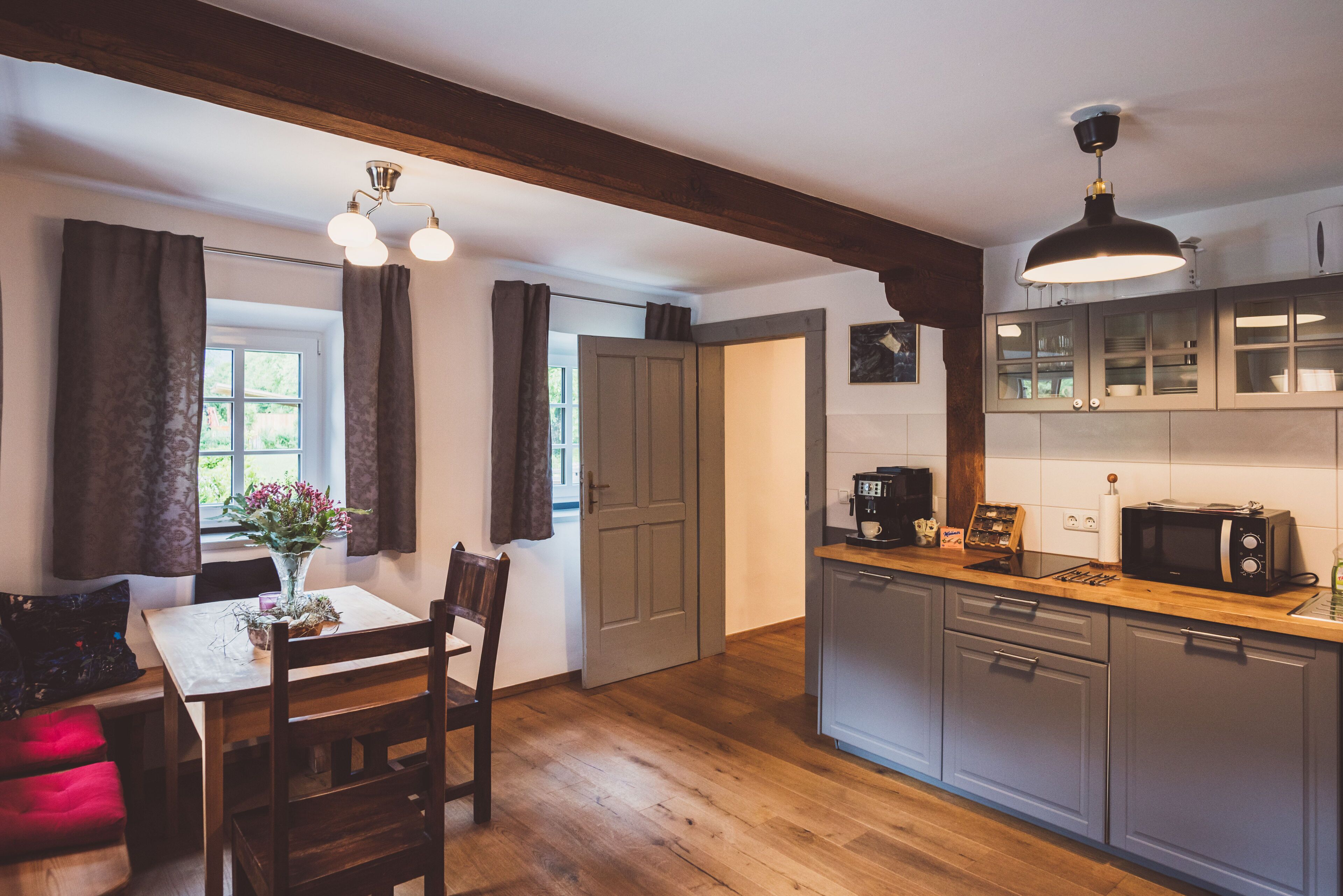 A kitchen with wooden cabinets, a dining table with chairs, a window with curtains, and a pendant light.