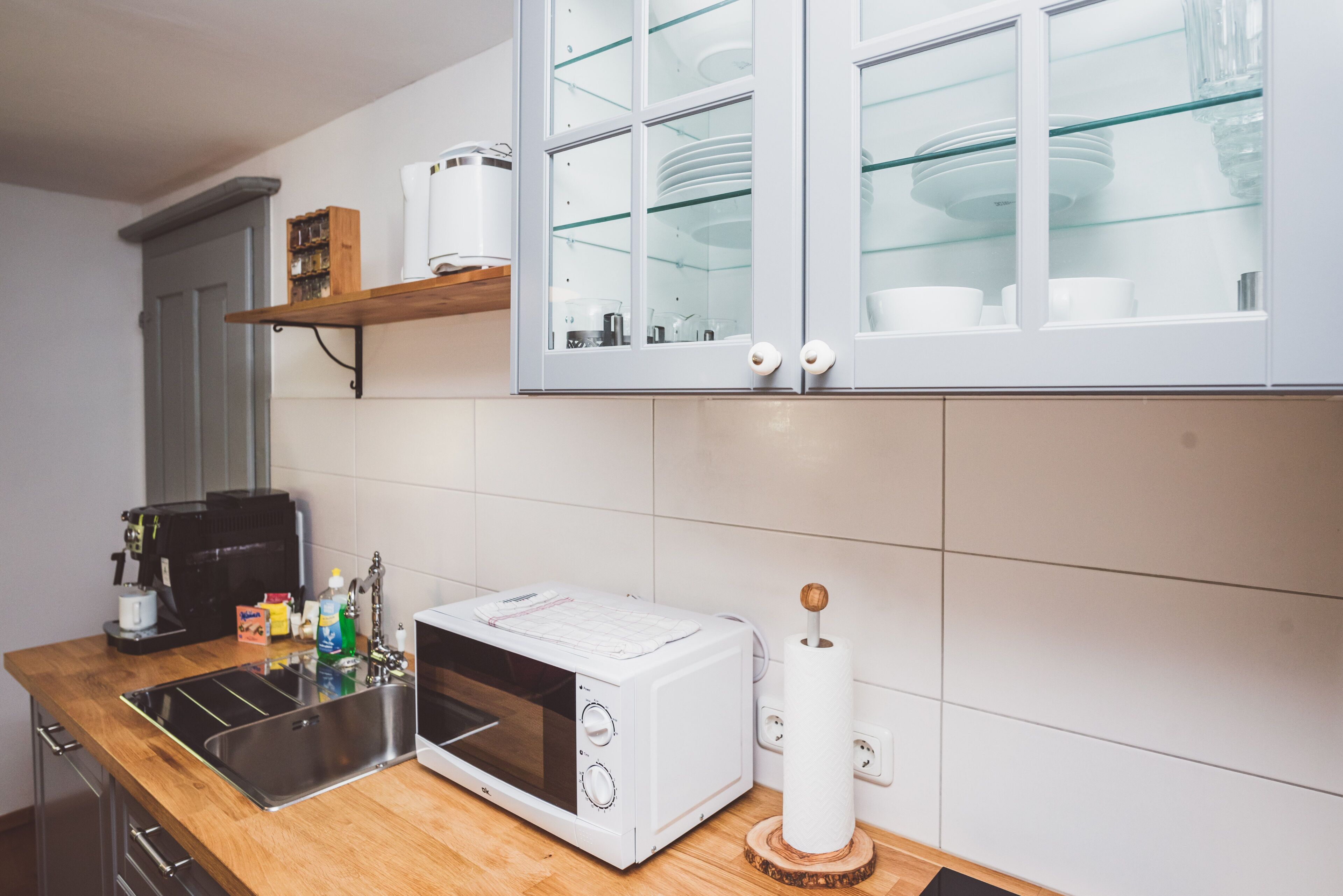 Een keuken met een magnetron, spoelbak en een plank met servies.