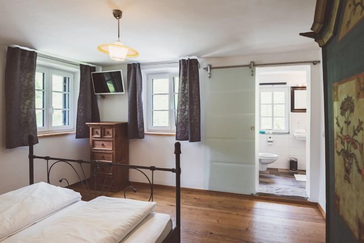 Un dormitorio con cama, cómoda de madera, televisor y baño visible a través de una puerta abierta.
