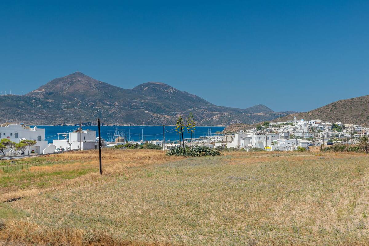 A coastal town with white buildings, a clear blue sea, and a mountain range in the background.
