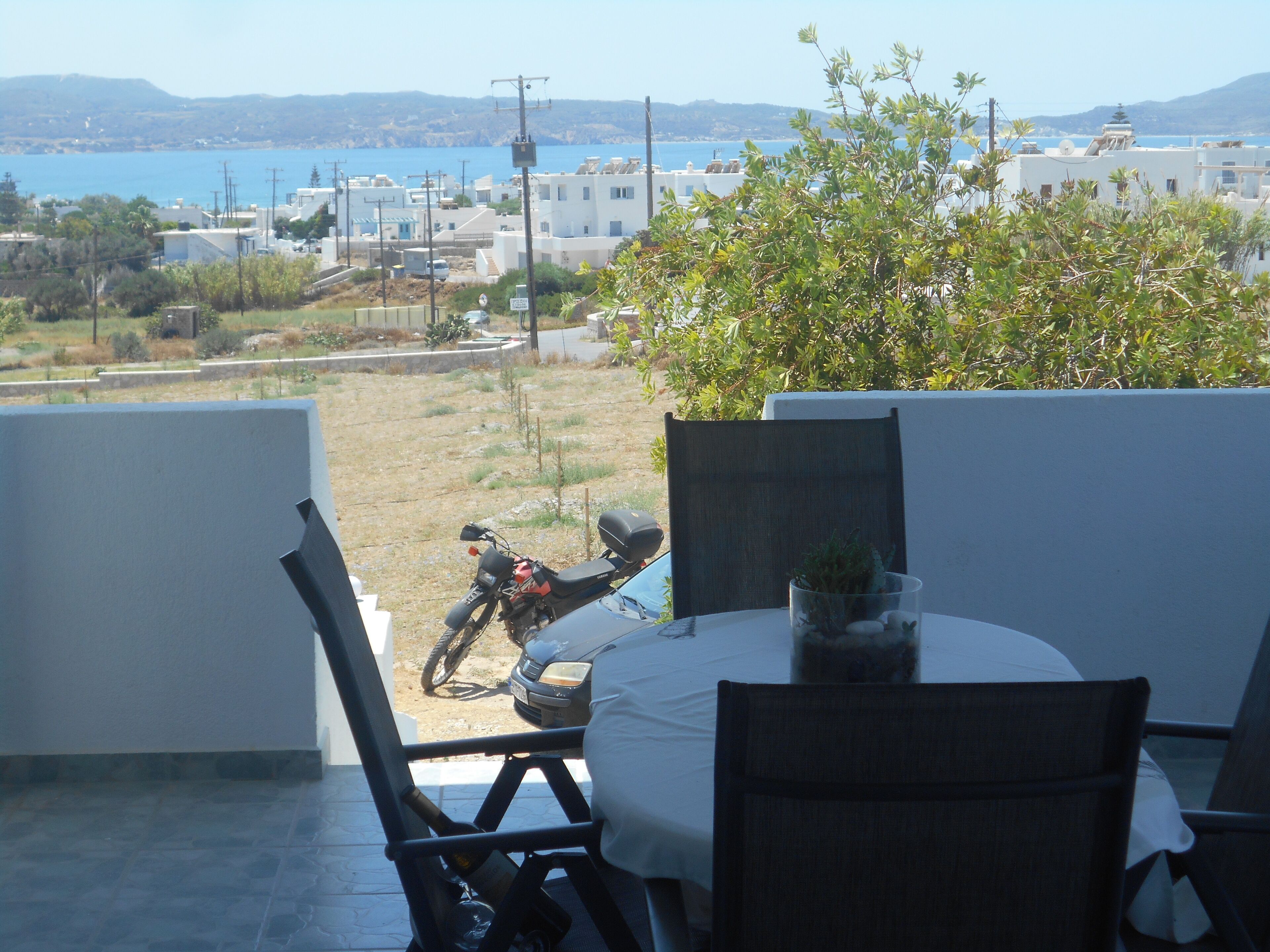 Varanda com mesa e cadeiras, com vista para a orla, edifícios e um mar aberto.