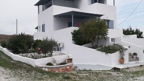 A modern white building with multiple balconies, a landscaped garden with a statue, and a gravel driveway. - Elea Milos (Milos)