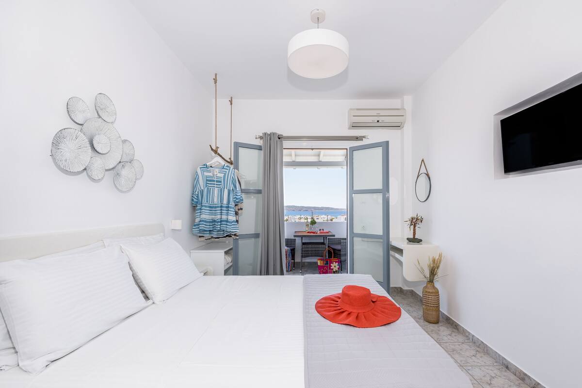 A modern hotel room with a bed, a TV, a balcony with a view, and a shower area.