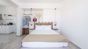 A modern bedroom with a large bed, a wooden headboard, a bedside table, a nightstand, and a small kitchen area with a sink and a coffee maker. - Elea Milos (Milos)