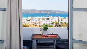 A balcony with a table set for two, overlooking a coastal town with white buildings and a clear blue sea. - Elea Milos (Milos)