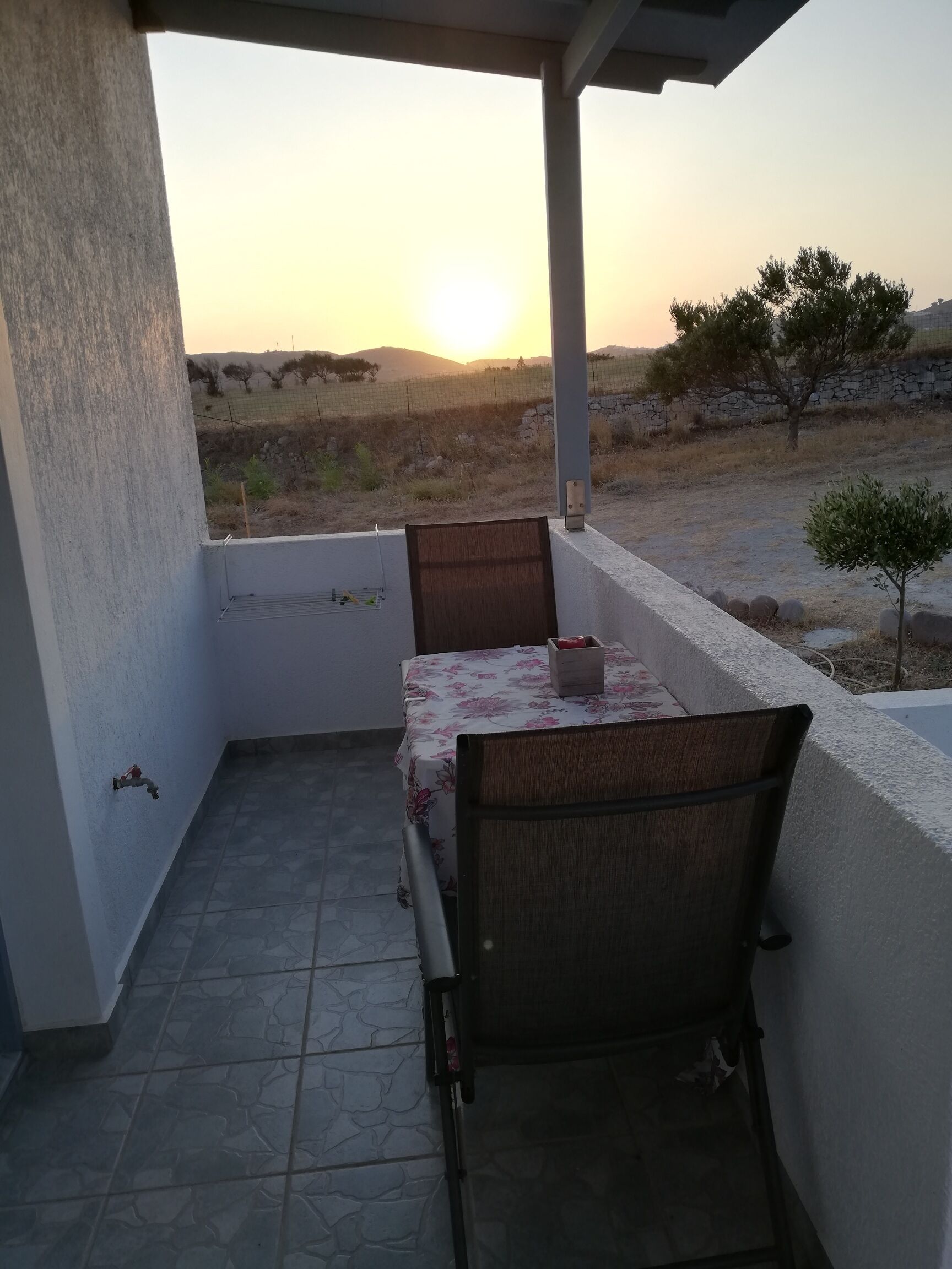 Un espace extérieur abrité, avec une table et des chaises, d’où l’on peut admirer le coucher du soleil, et un mur en pierre.