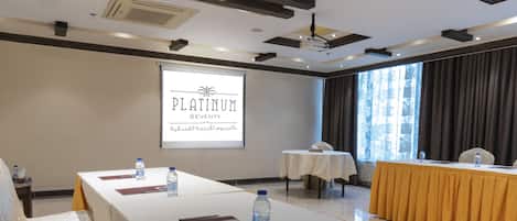 A conference room with a long table, water bottles, and a projector screen displaying "PLATINUM SEVENTY".
